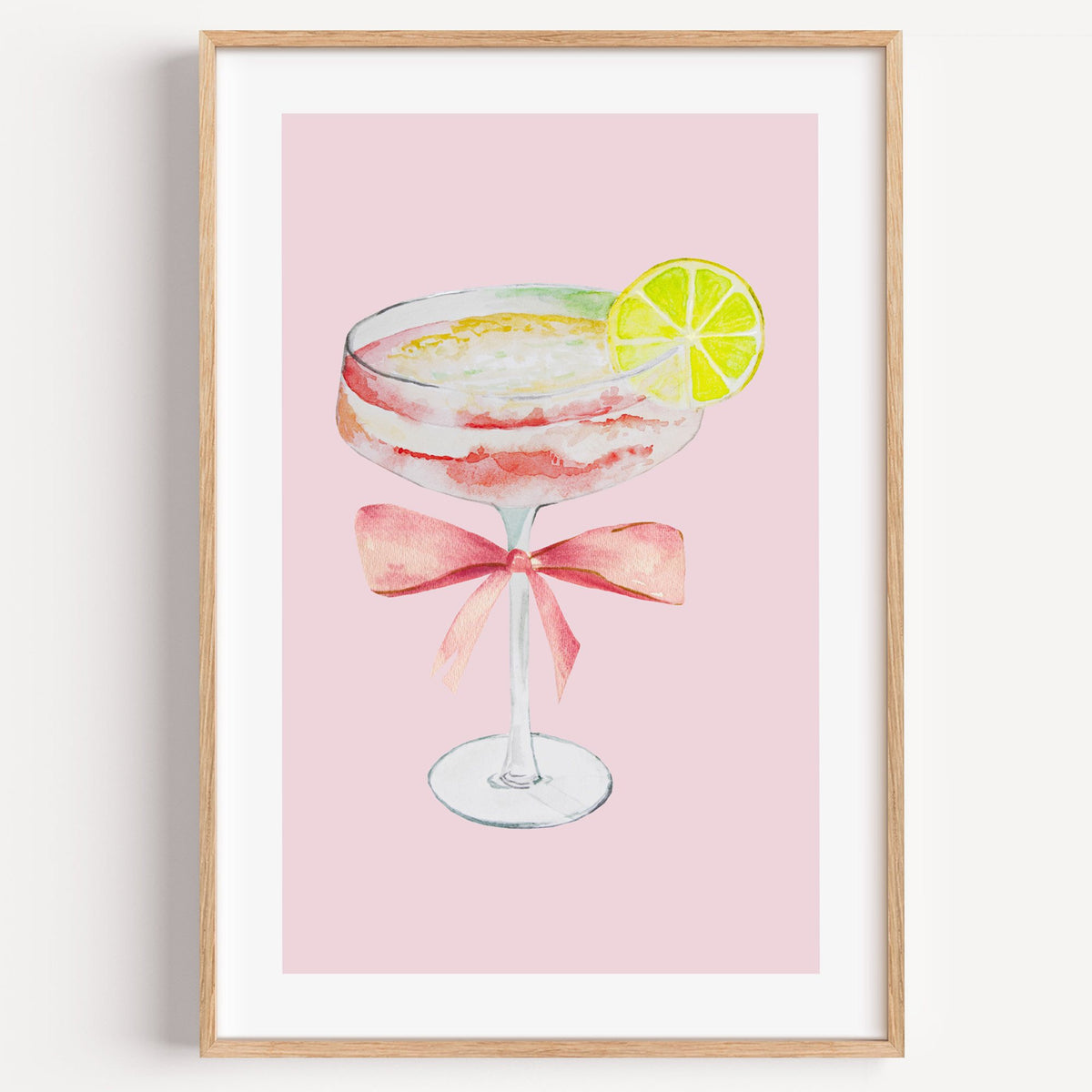 lime coupe cocktail pink bow watercolor print in a light oak frame on a plain white wall