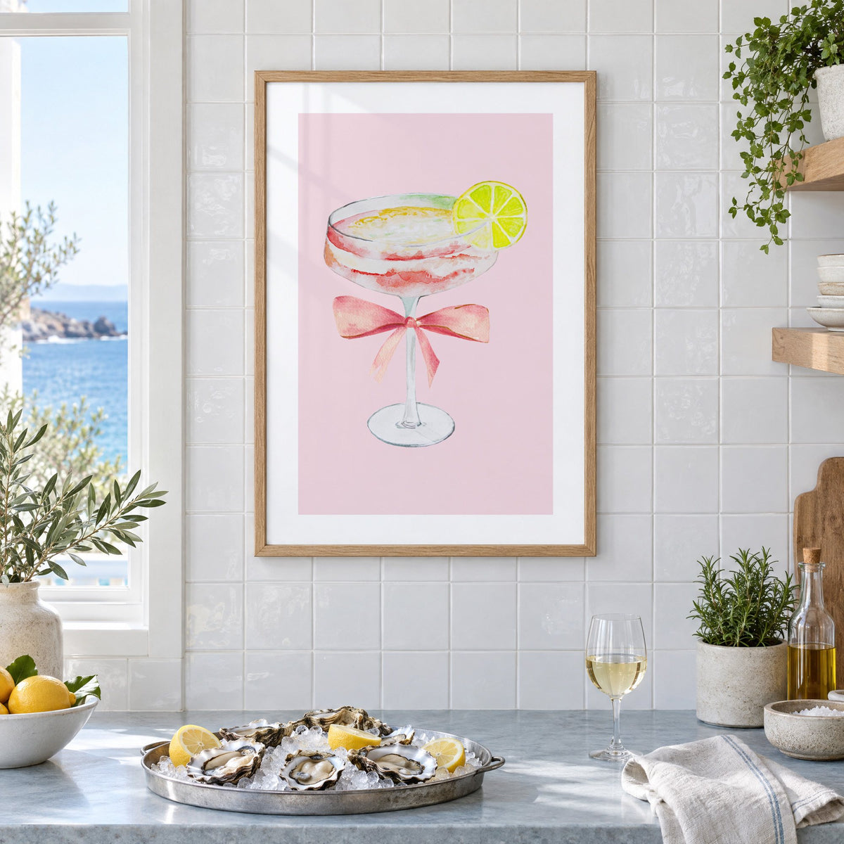 lime coupe cocktail pink bow watercolor print in an oak frame on white tiles above a marble counter with oysters and lemons by a sea view