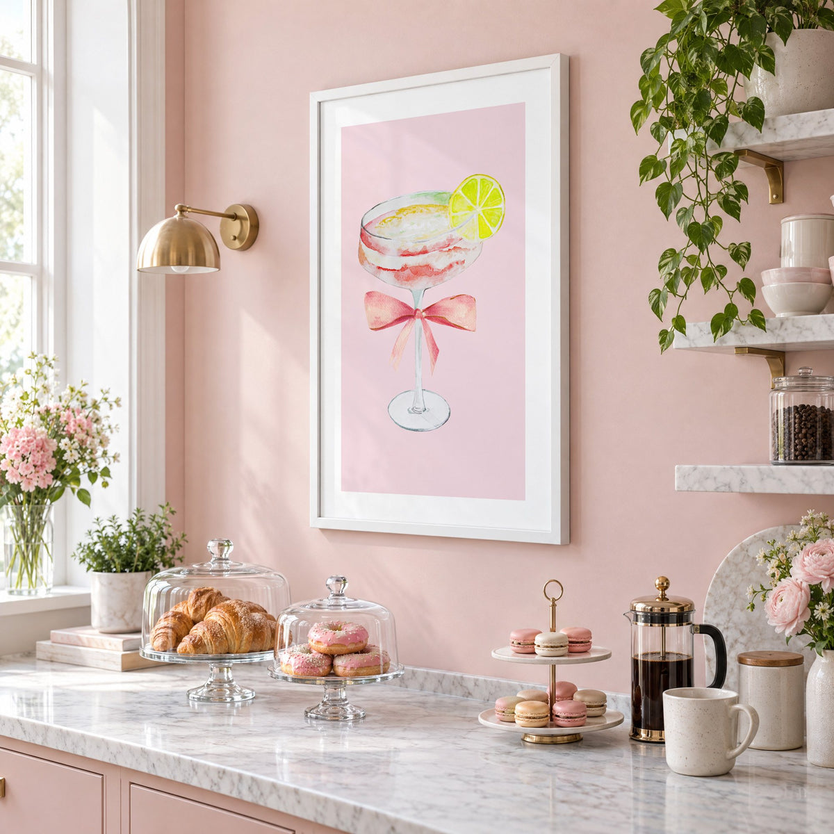 lime coupe cocktail pink bow watercolor print in a white frame on a blush pink wall above a patisserie counter with croissants and macarons, seen at an angle
