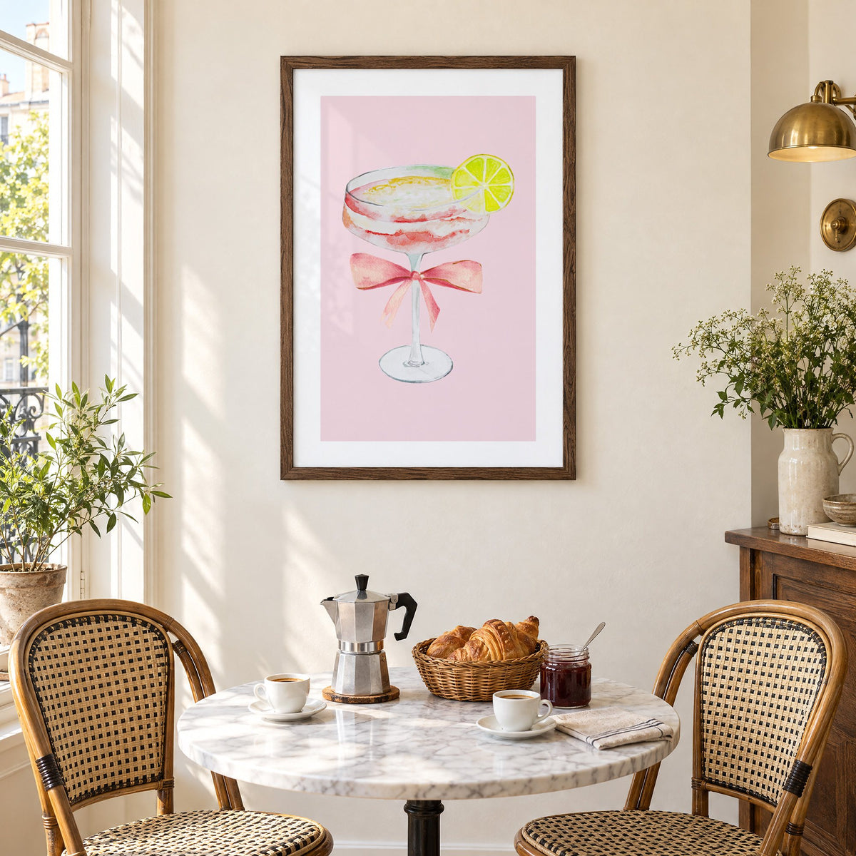 lime coupe cocktail pink bow watercolor print in a walnut frame above a marble bistro table with croissants and rattan chairs