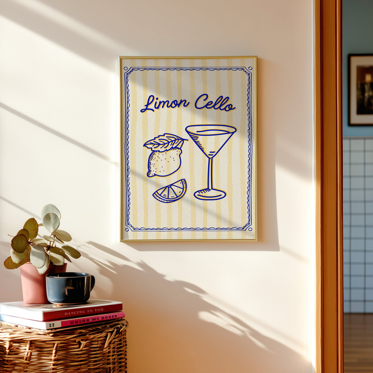 Limoncello martini print shown in a gold frame above a basket of books and a pilea plant