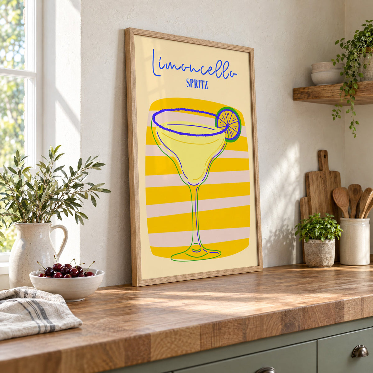 Limoncello Spritz yellow stripe print in an oak frame leaning on a butcher block island beside a bowl of cherries