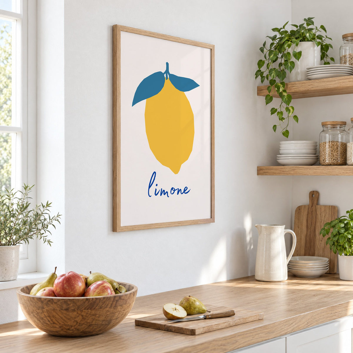 limone yellow cut-paper lemon print in an oak frame on a white kitchen wall above a counter with apples and pears, seen at an angle