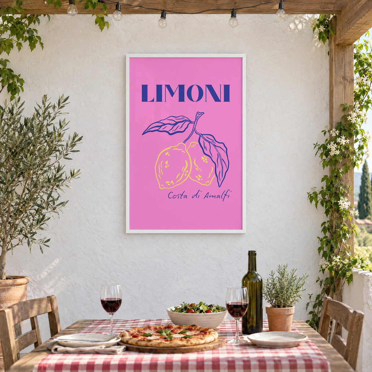 LIMONI Costa di Amalfi lemon branch print in a white frame on a stucco wall above a checked-cloth table with pizza and red wine