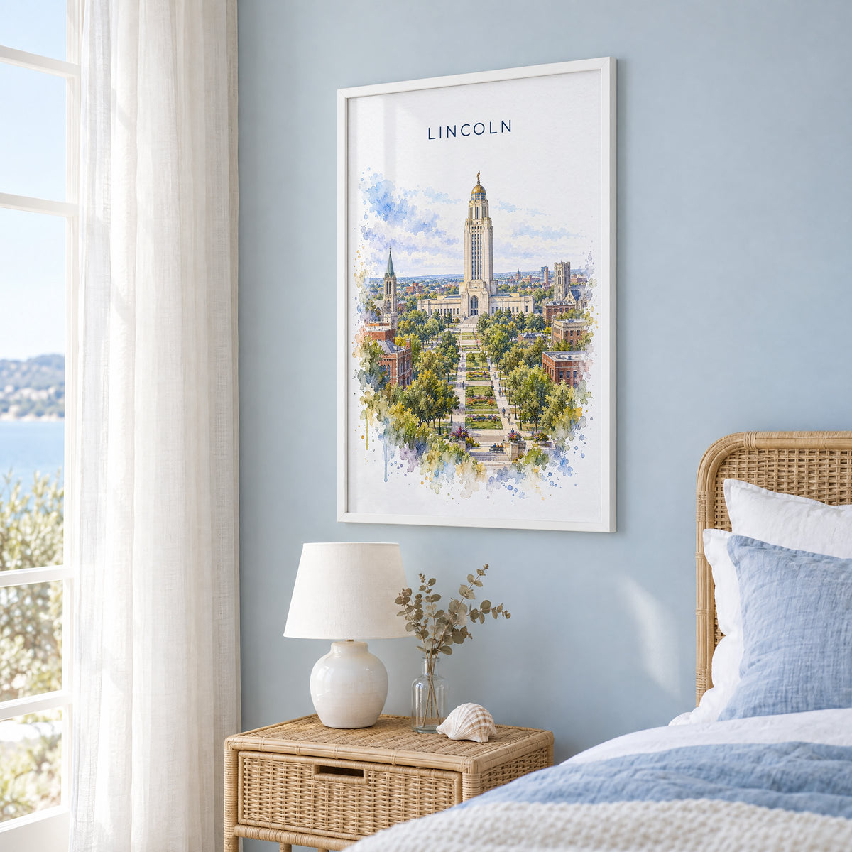 Lincoln, Nebraska watercolor print in a white frame on a pale blue wall beside a rattan bed in a coastal bedroom
