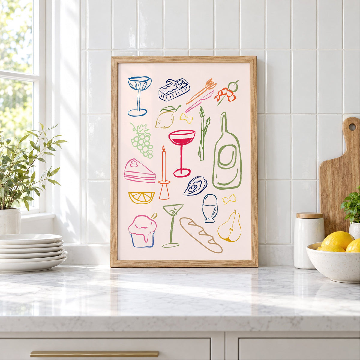 Line art candle coupe dinner party print in an oak frame leaning on a marble counter by white tiles and lemons