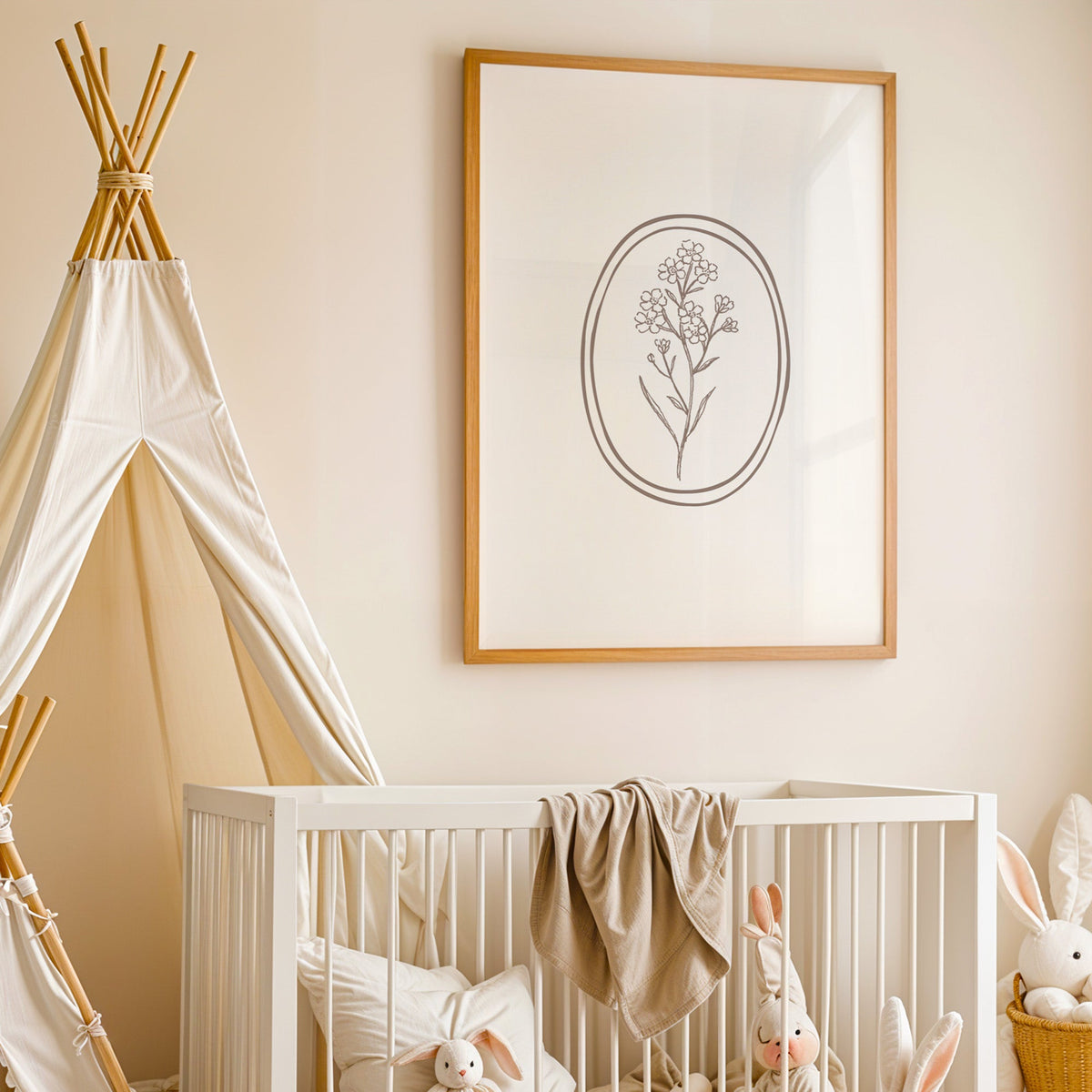 Line art flower sprig in a double oval nursery print in an oak frame above a white crib beside a canvas teepee