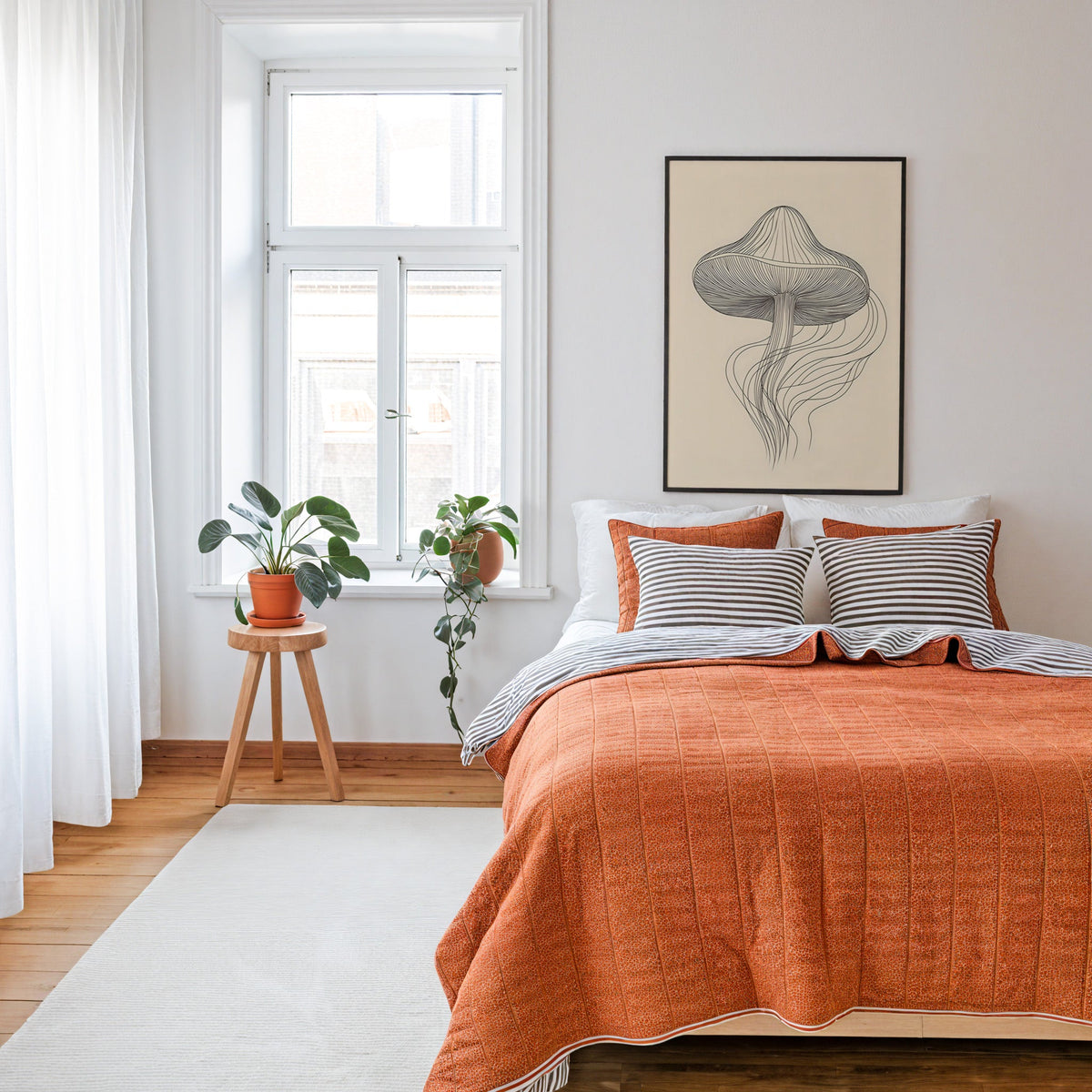 Line art mushroom with flowing lines print in a thin black frame above a bed with a rust orange quilt