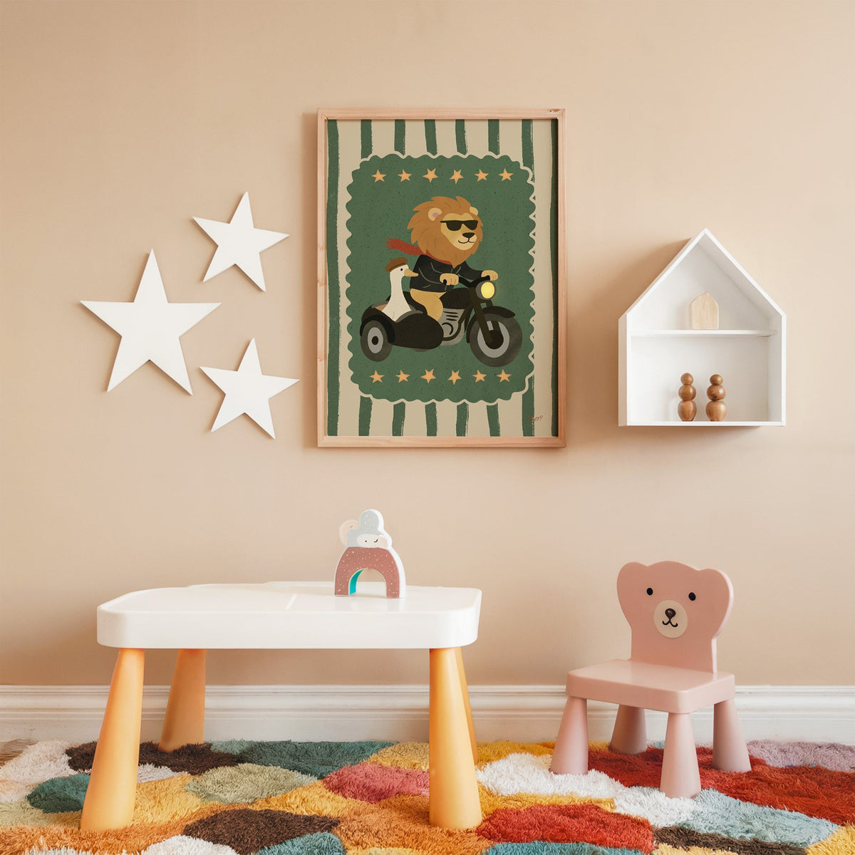Lion on motorcycle with goose sidecar nursery print in an oak frame on a peach wall above a kids table with wall stars
