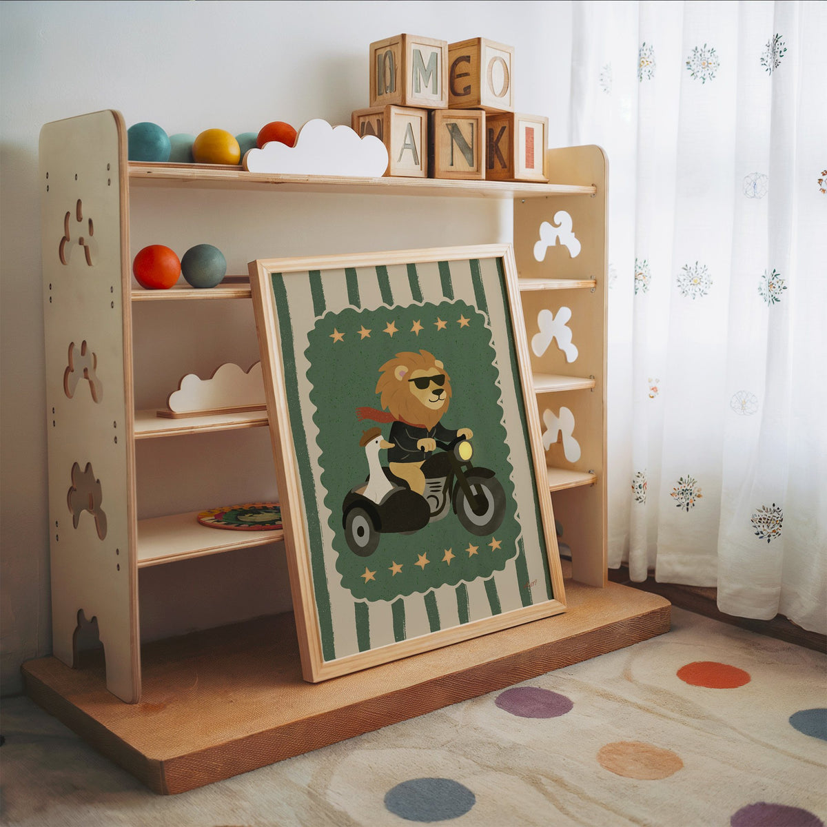 Lion on motorcycle with goose sidecar nursery print in an oak frame leaning on a toy shelf with wooden letter blocks