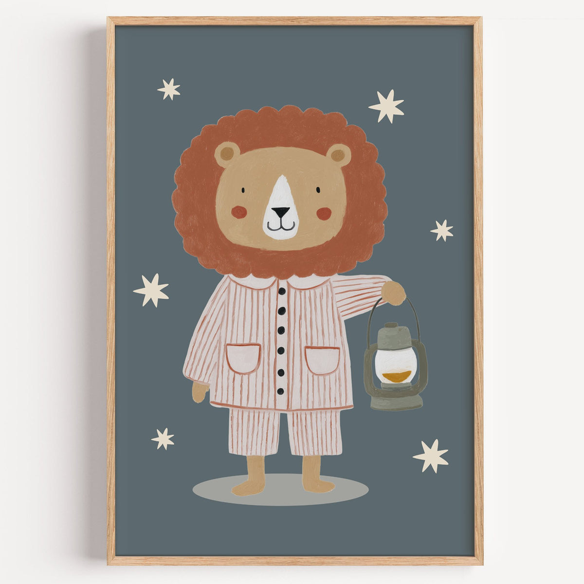 Lion in pajamas with lantern nursery print in a light oak frame on a plain white wall