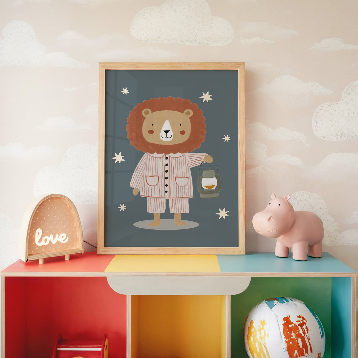 Lion in pajamas with lantern nursery print in an oak frame on a rainbow toy shelf against cloud wallpaper