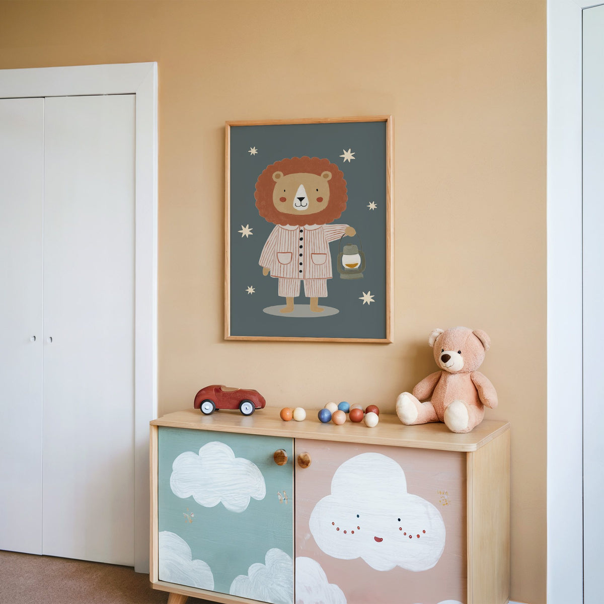 Lion in pajamas with lantern nursery print in an oak frame on a peach wall above a cloud-painted cabinet
