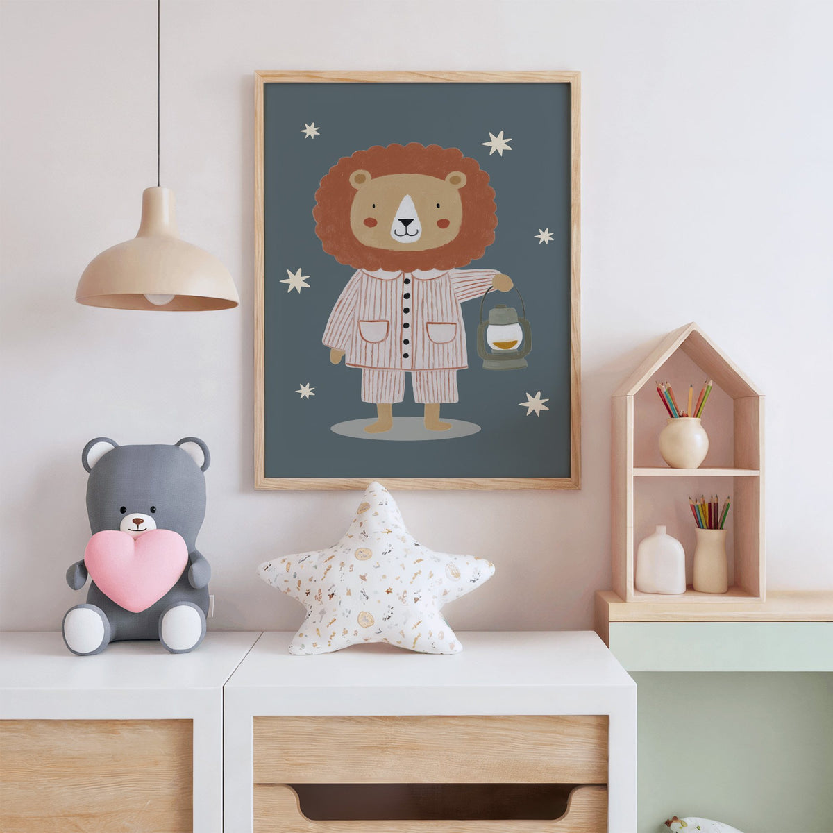 Lion in pajamas with lantern nursery print in an oak frame above a white dresser with a star pillow and house shelf