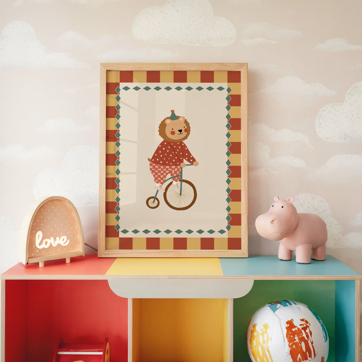 Lion penny-farthing circus nursery print in an oak frame on a rainbow toy shelf against cloud wallpaper