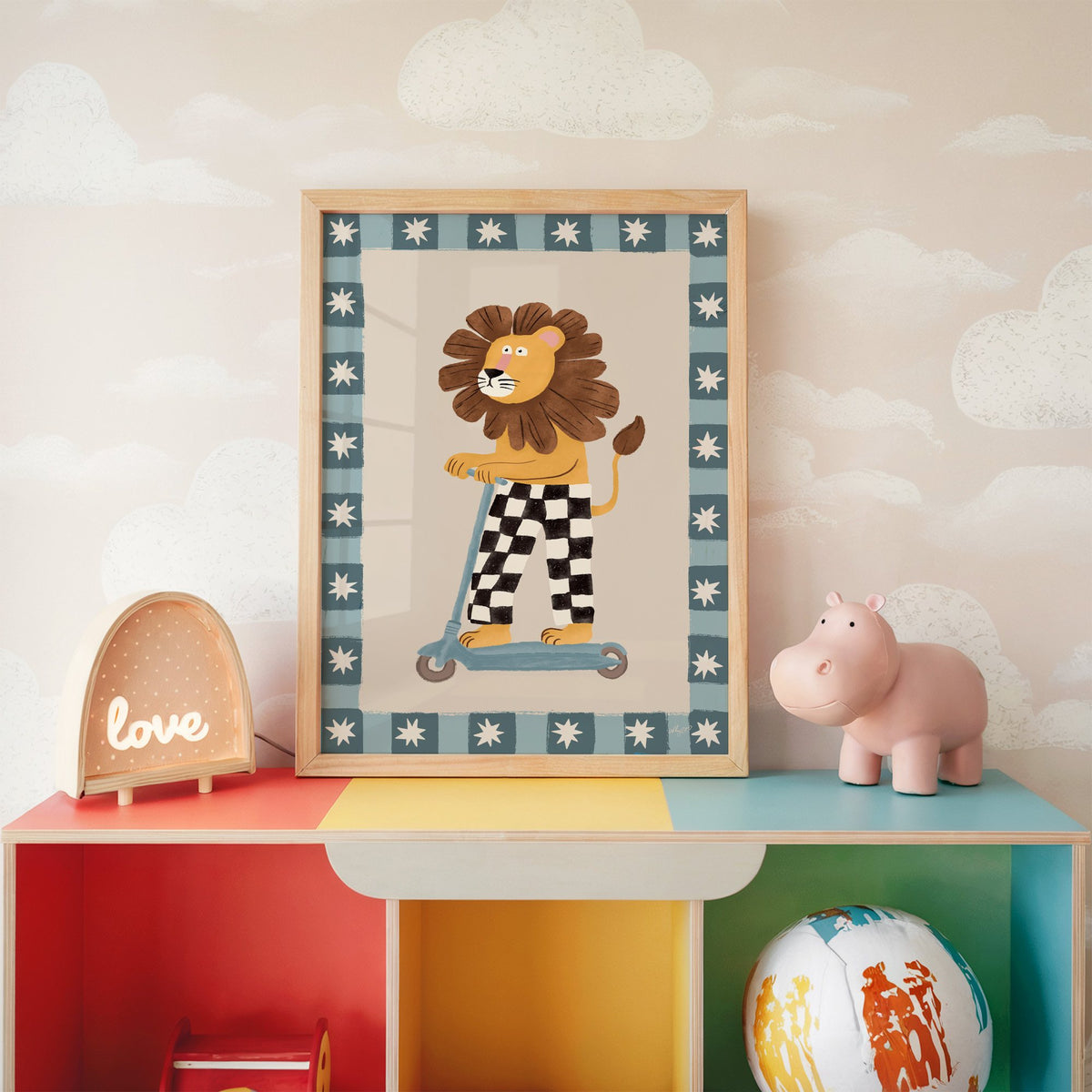 Lion on scooter in checkered pants nursery print in an oak frame on a rainbow toy shelf against cloud wallpaper