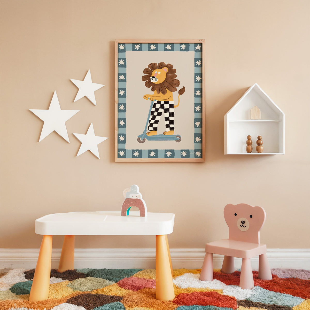 Lion on scooter in checkered pants nursery print in an oak frame on a peach wall above a kids table with wall stars