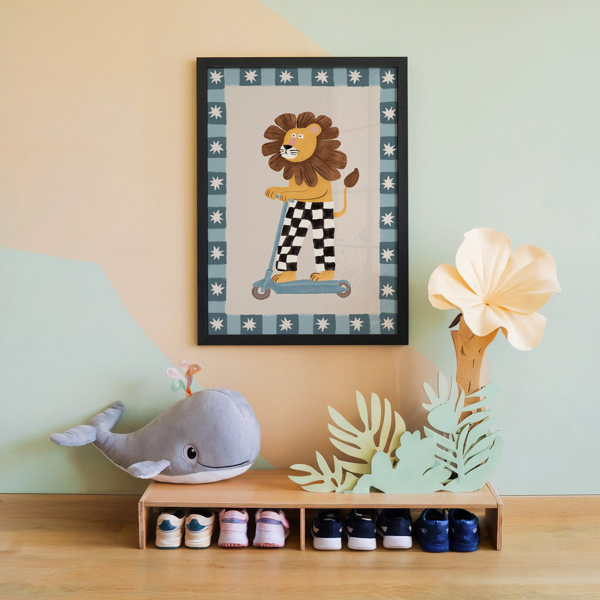 Lion on scooter in checkered pants nursery print in a black frame on a mint and peach wall above a whale plush