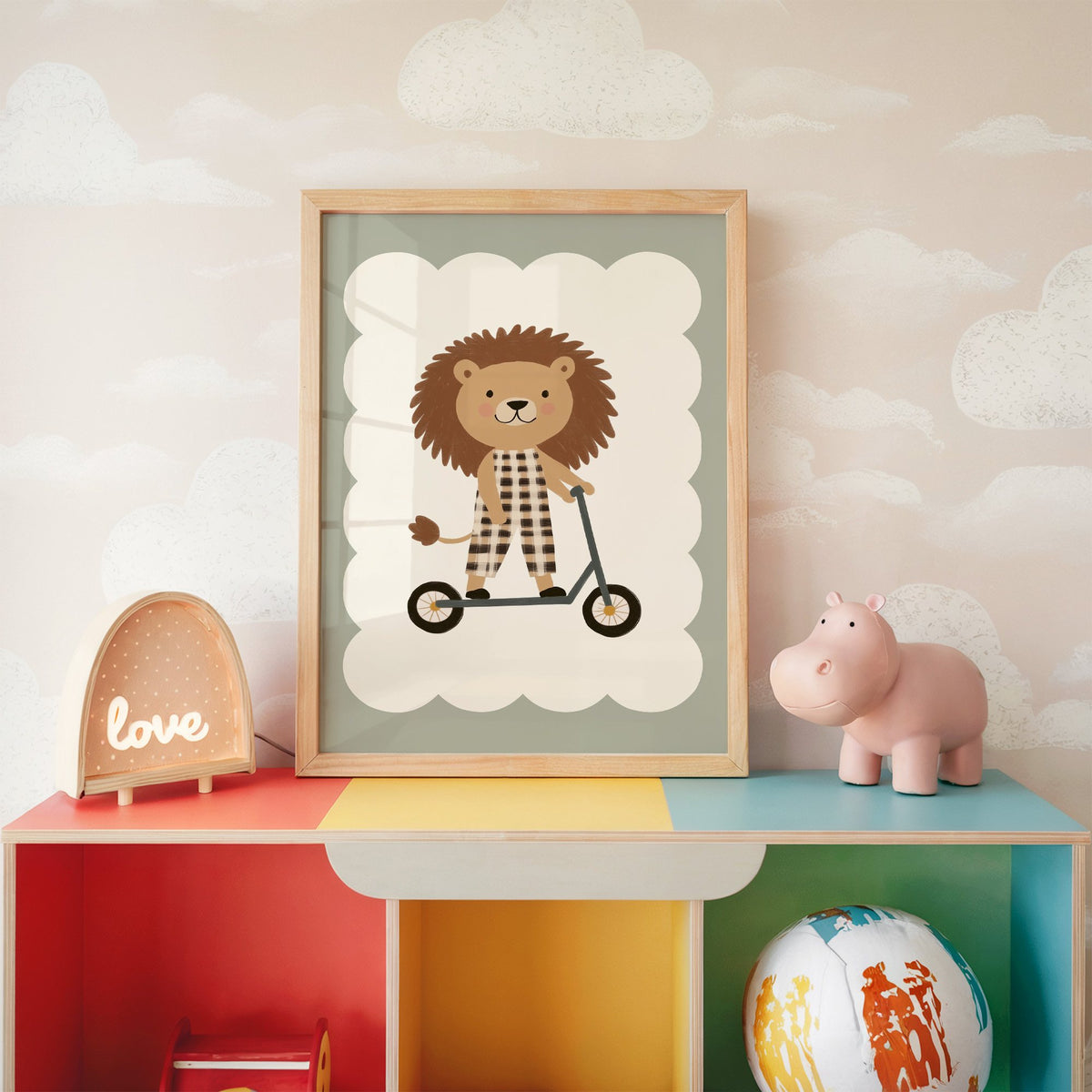 Lion on scooter gingham nursery print in an oak frame on a rainbow toy shelf against cloud wallpaper