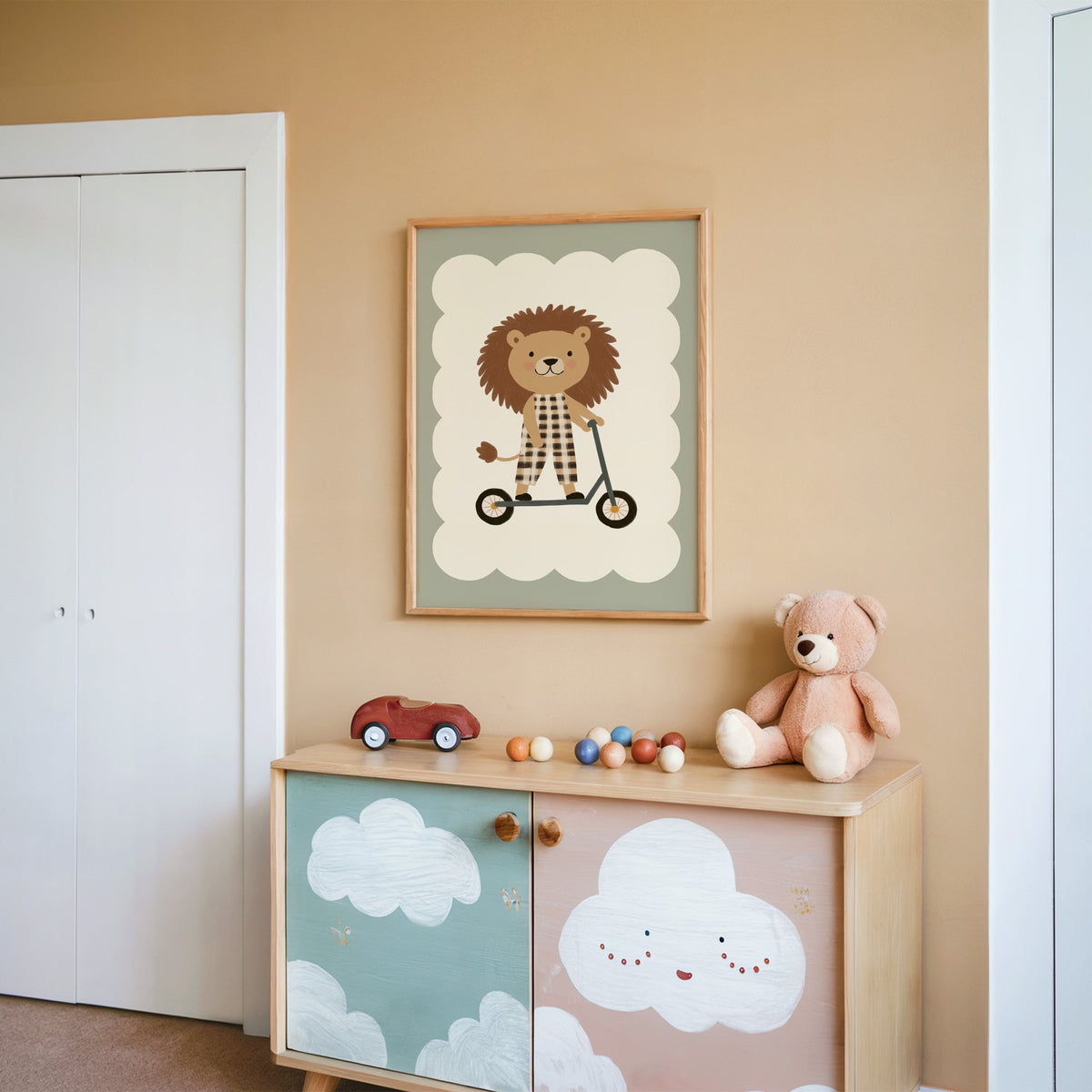 Lion on scooter gingham nursery print in an oak frame on a peach wall above a cloud-painted cabinet