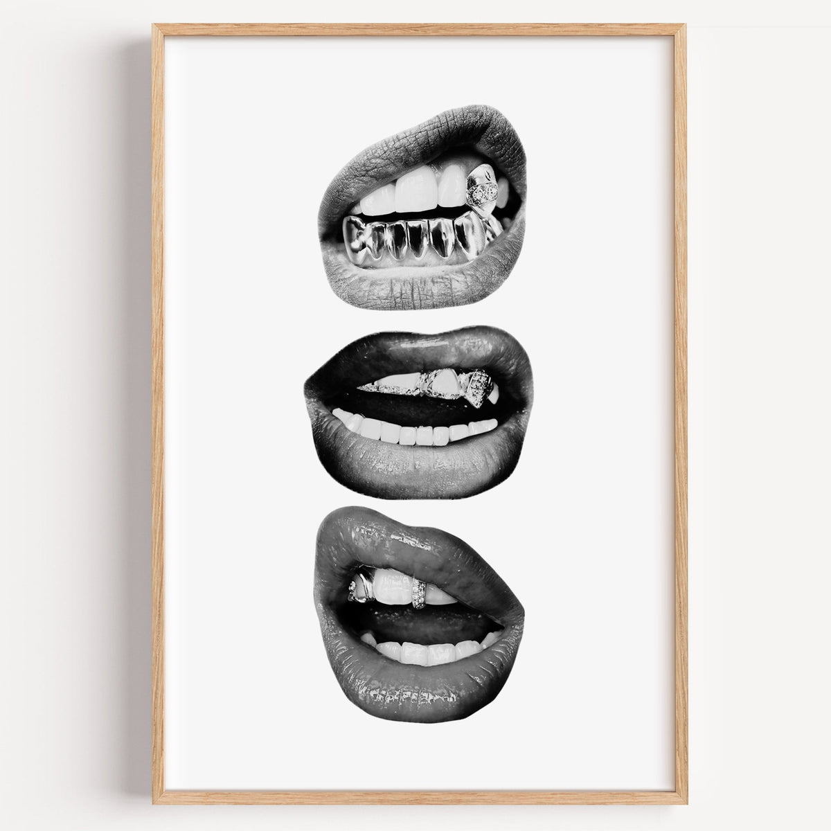 Three lips with jeweled metal grills print in a light oak frame on a plain white wall