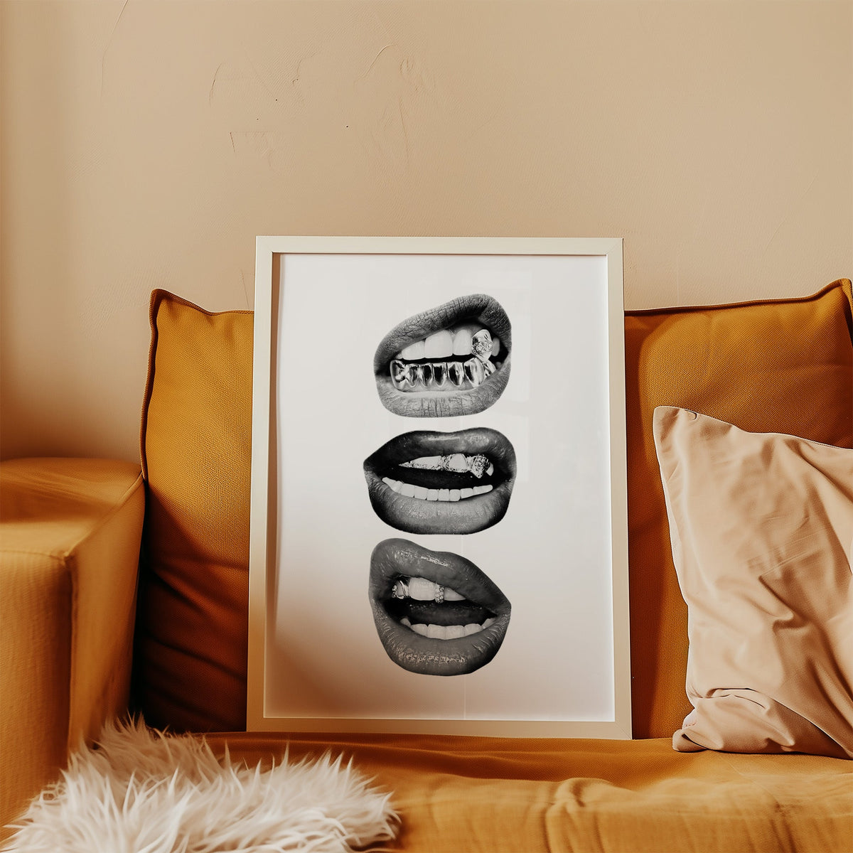 Three lips with jeweled metal grills print in a white frame leaning on a mustard velvet sofa