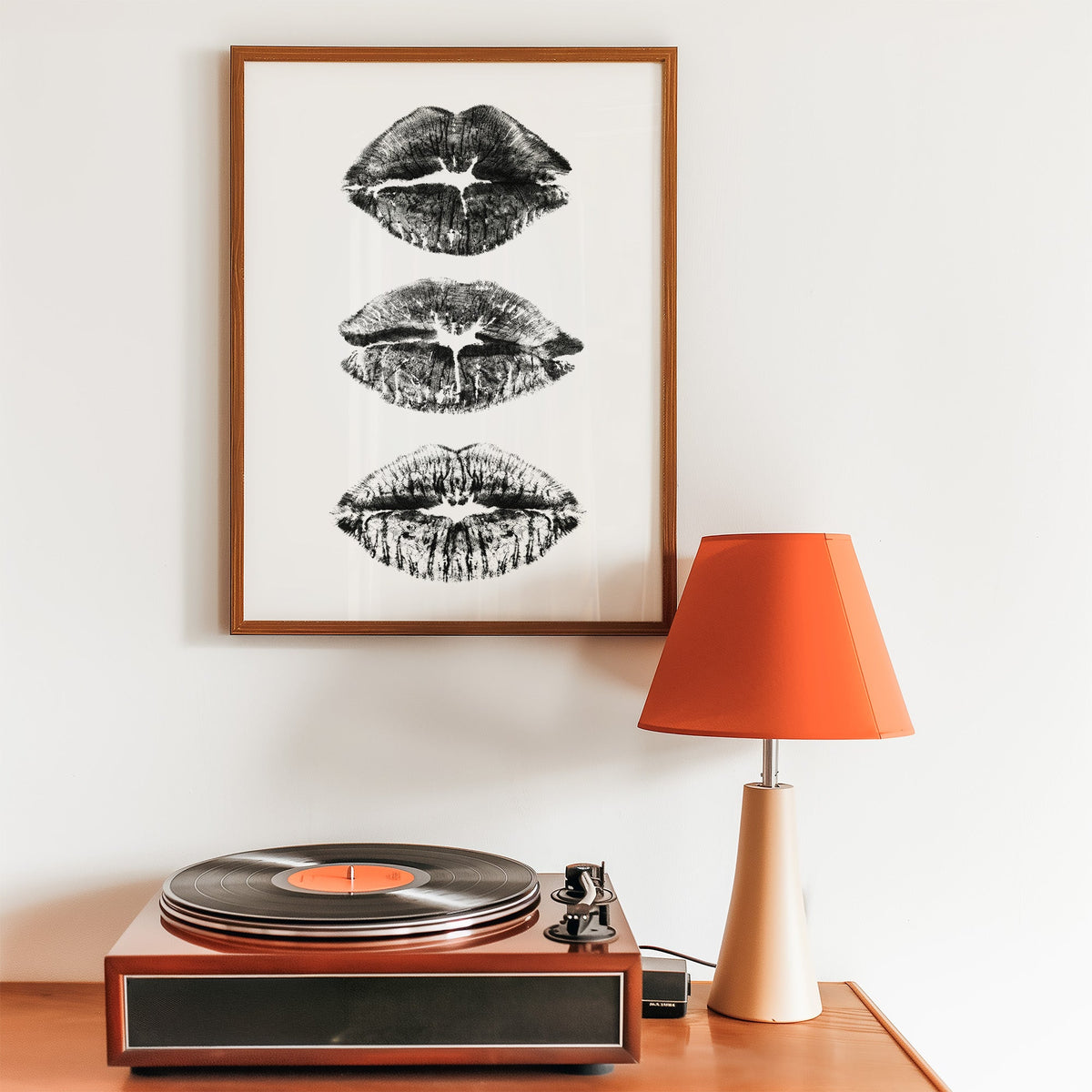 Three lipstick kiss marks stacked print in a walnut frame above a record player and orange lamp