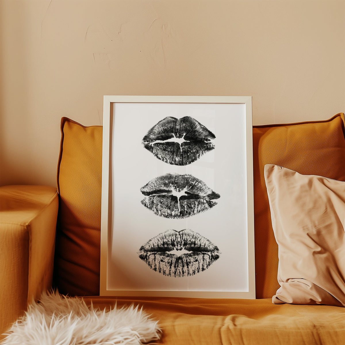 Three lipstick kiss marks stacked print in a white frame leaning on a mustard velvet sofa