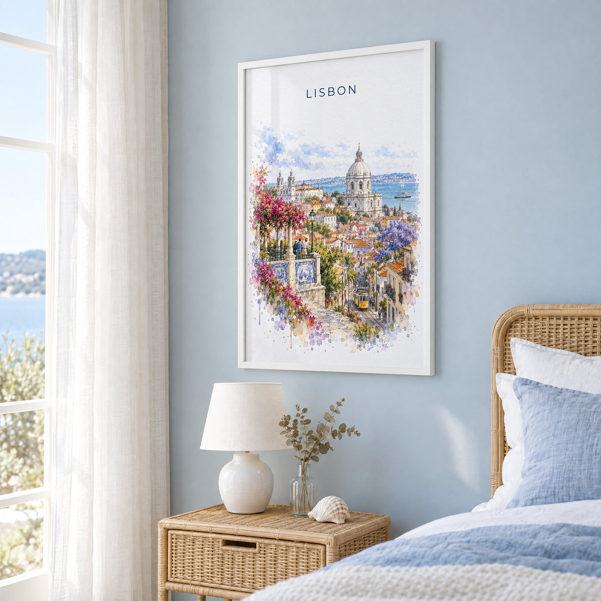 Lisbon watercolor print in a white frame on a pale blue wall beside a rattan bed in a coastal bedroom