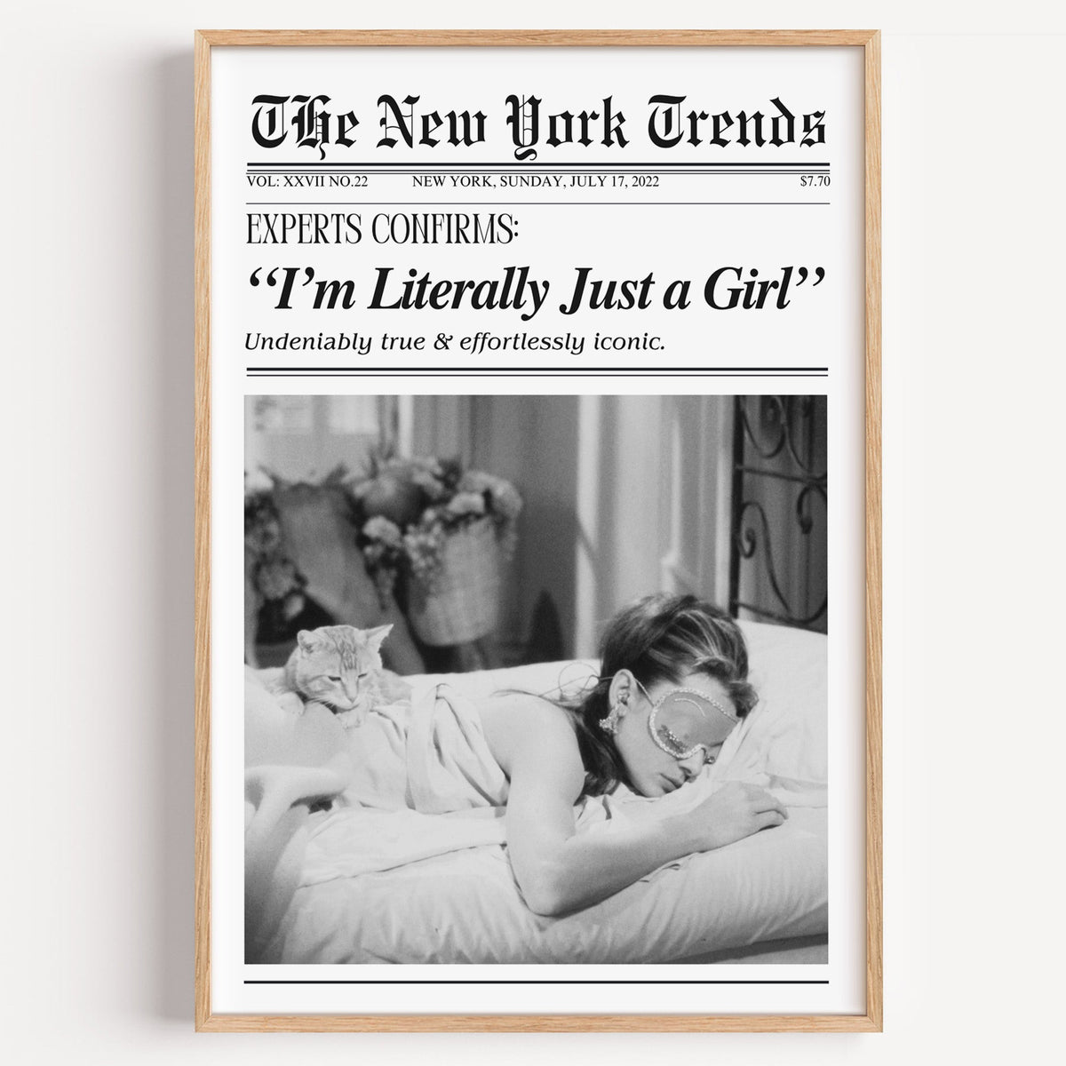 Woman asleep beside tabby cat mock newspaper print in a light oak frame on a plain white wall