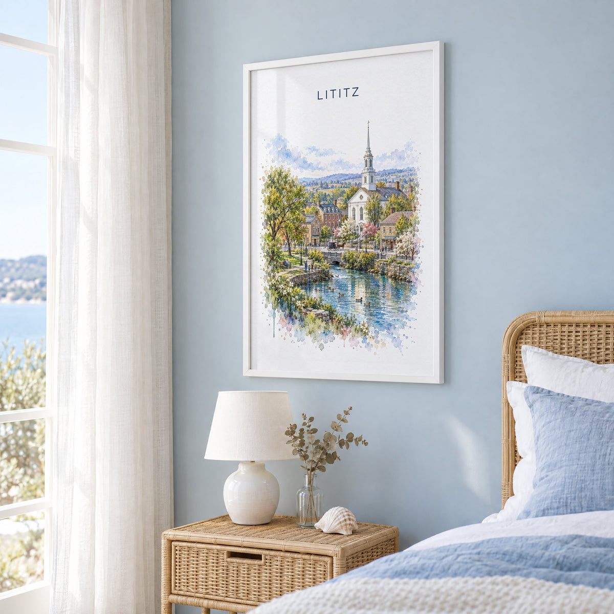Lititz, Pennsylvania watercolor print in a white frame on a pale blue wall beside a rattan bed in a coastal bedroom