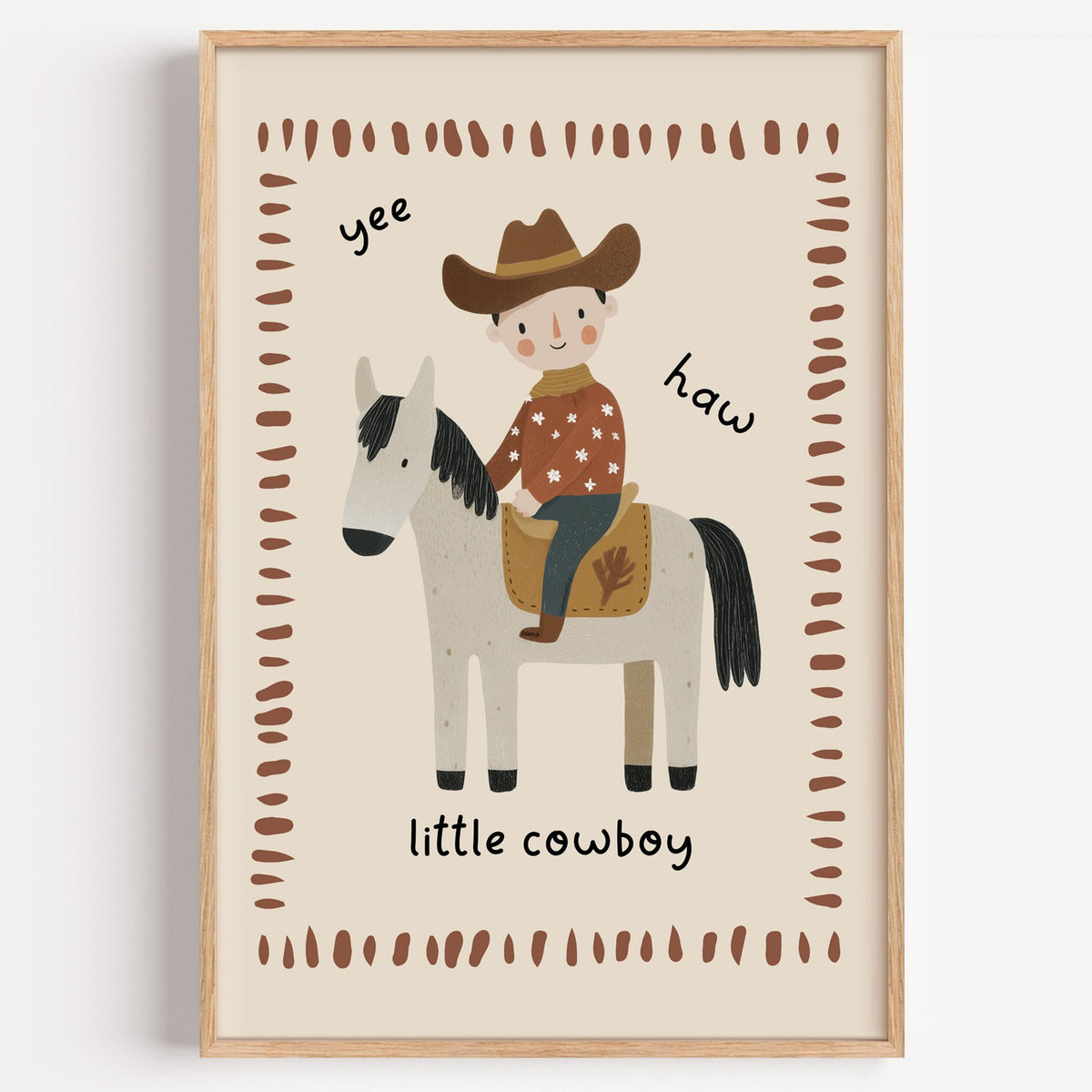 Little cowboy on horse yee haw nursery print in a light oak frame on a plain white wall