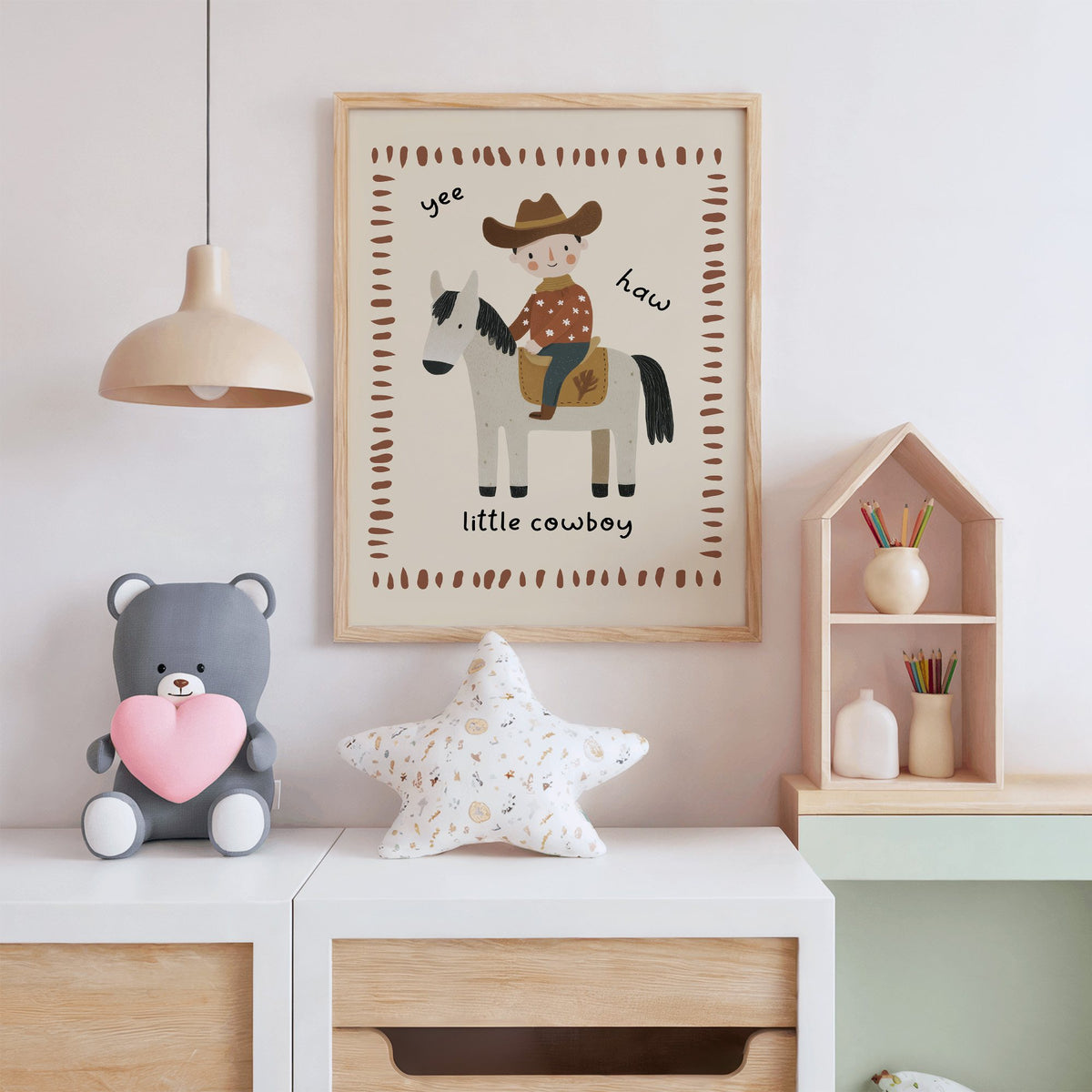 Little cowboy on horse yee haw nursery print in an oak frame above a white dresser with a star pillow and house shelf