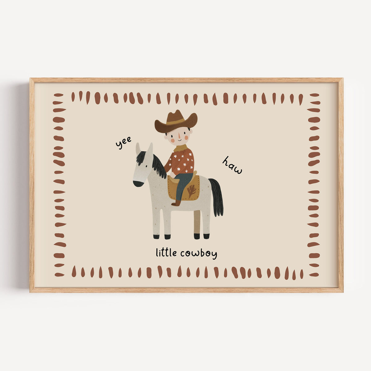 Landscape little cowboy on horse yee haw nursery print in a light oak frame on a plain white wall