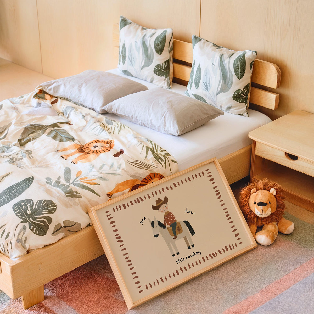 Landscape little cowboy on horse yee haw nursery print in an oak frame leaning on a kids bed by a lion plush