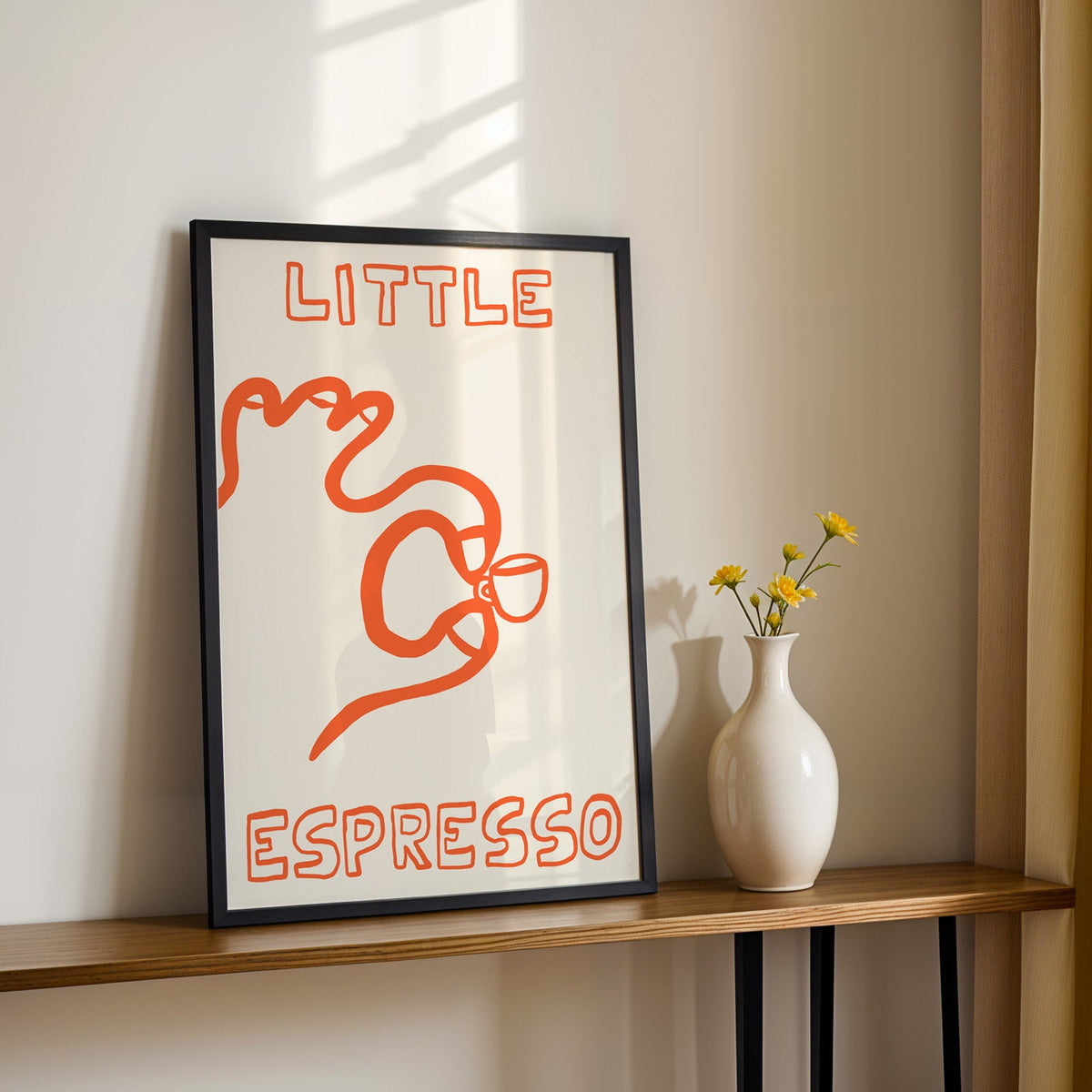 Little espresso one line print in a black frame on a console table with yellow daisies