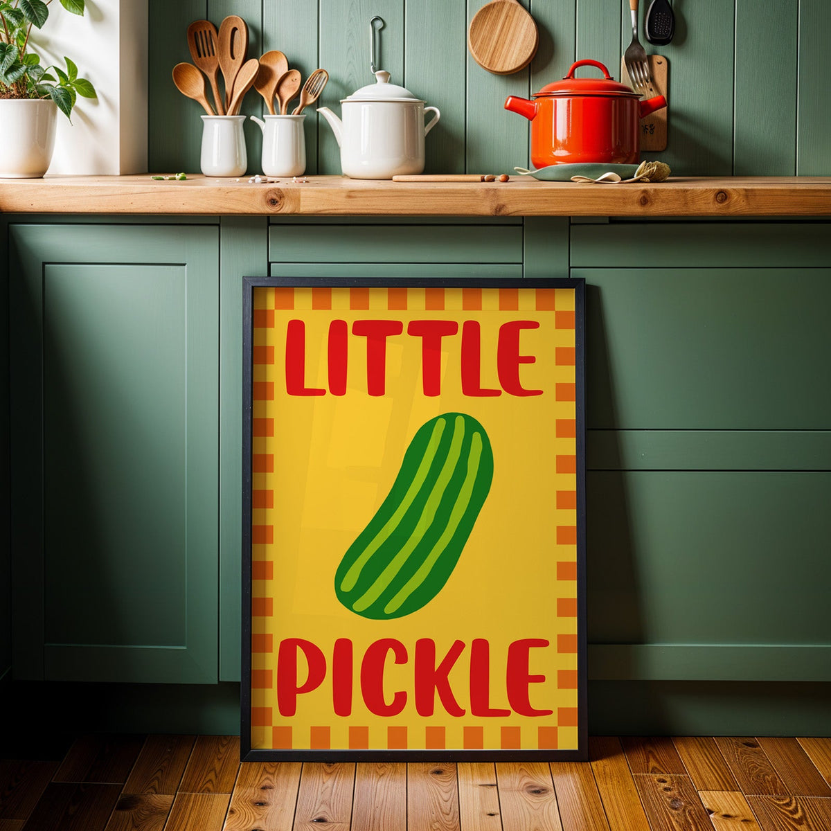 Little pickle print in a black frame against sage green kitchen cabinets