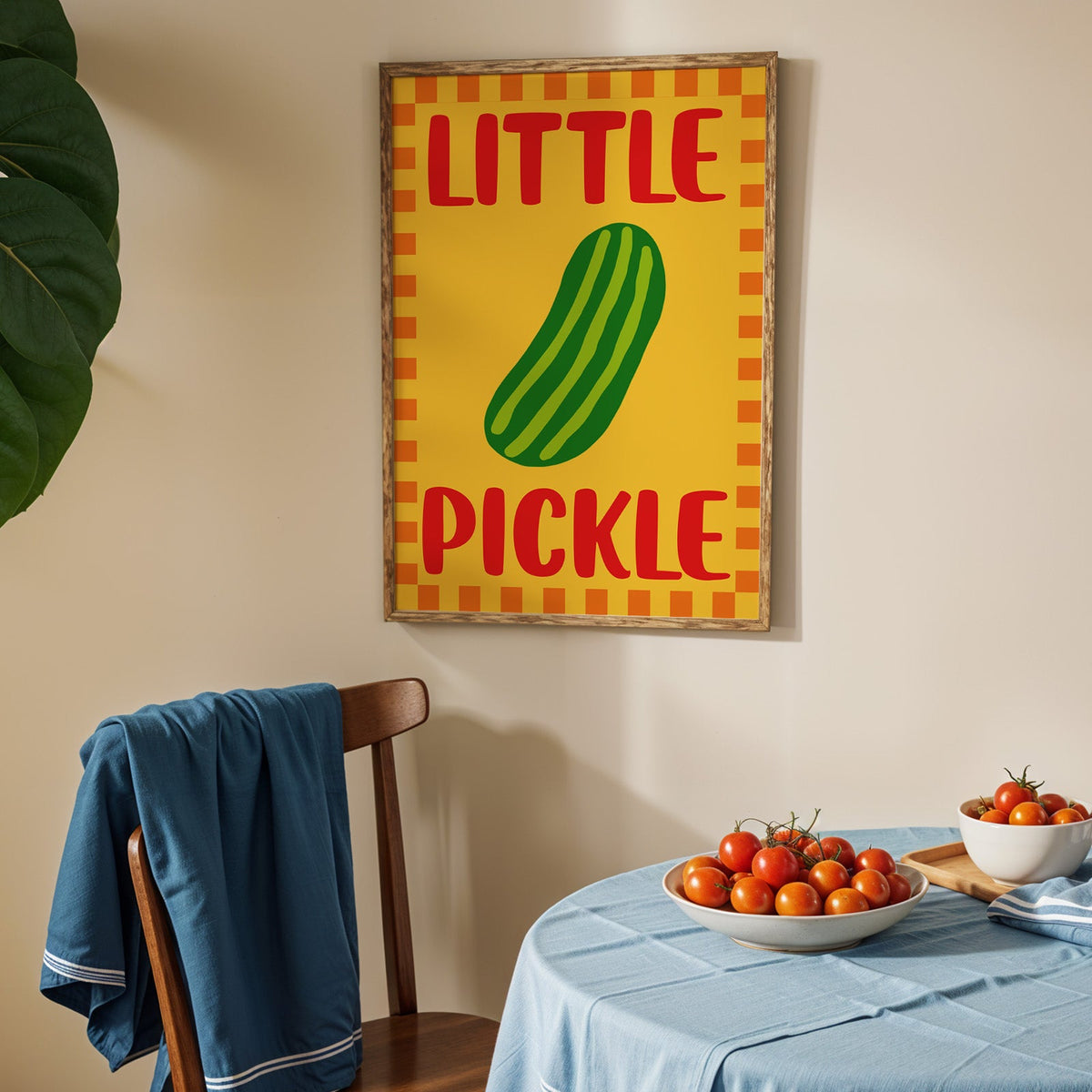 Little pickle print in an oak frame above a blue linen table with ripe tomatoes