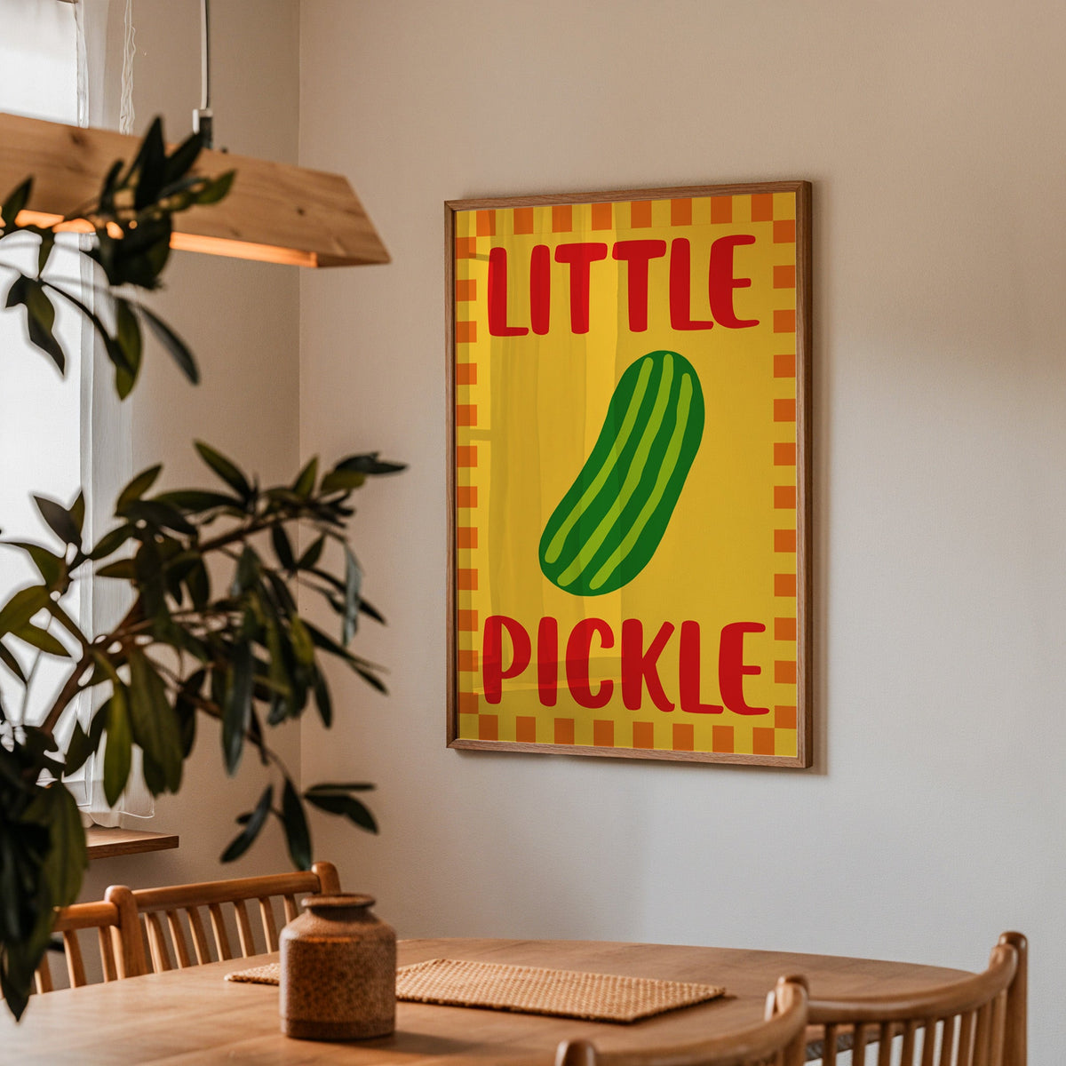 Little pickle print in a walnut frame above a dining table beside an olive tree