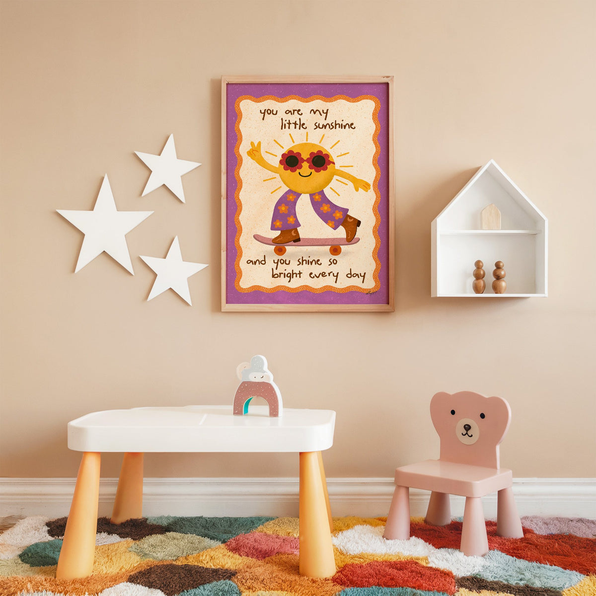 Skateboarding sun little sunshine nursery print in an oak frame on a peach wall above a kids table with wall stars