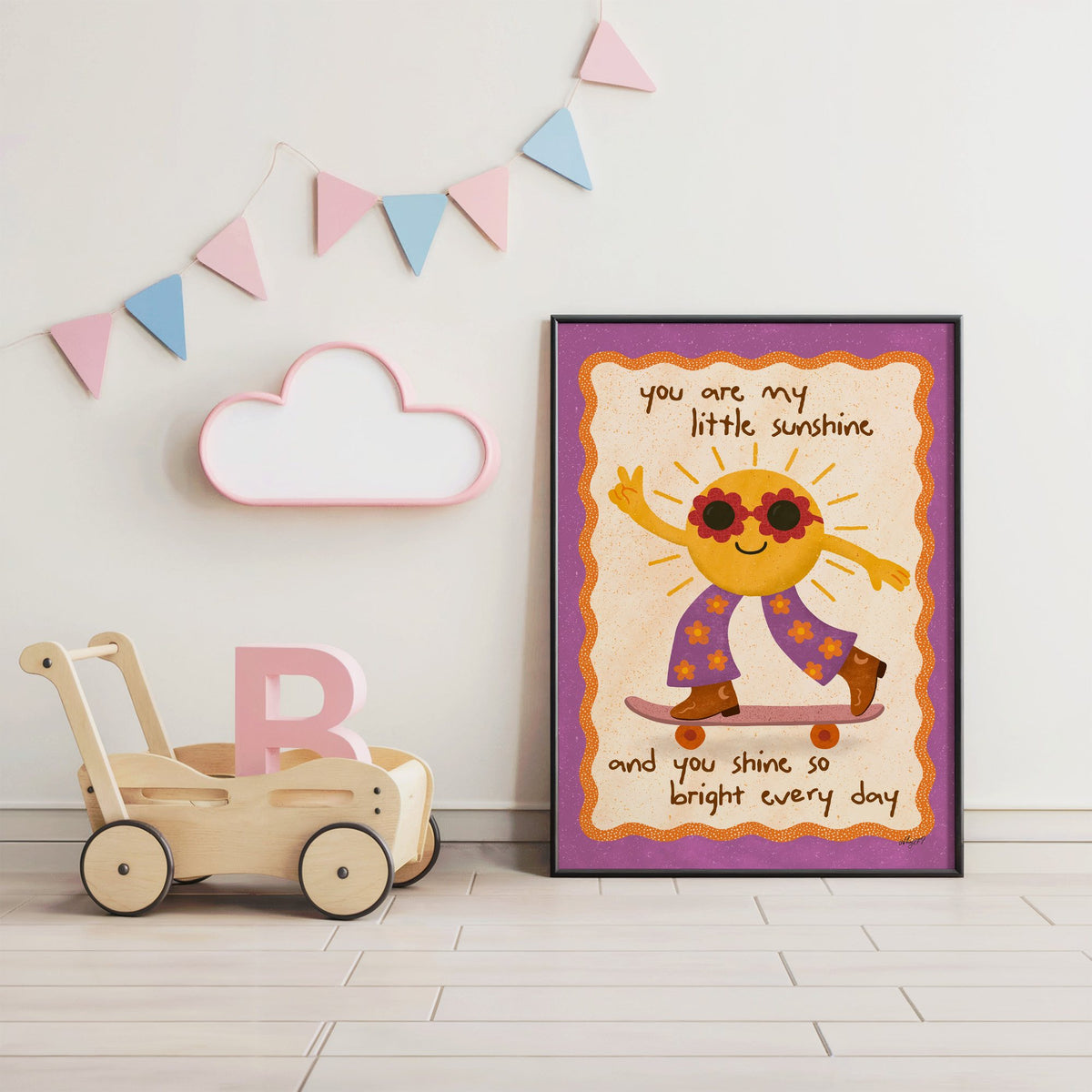 Skateboarding sun little sunshine nursery print in a black frame under pastel bunting by a wooden baby walker