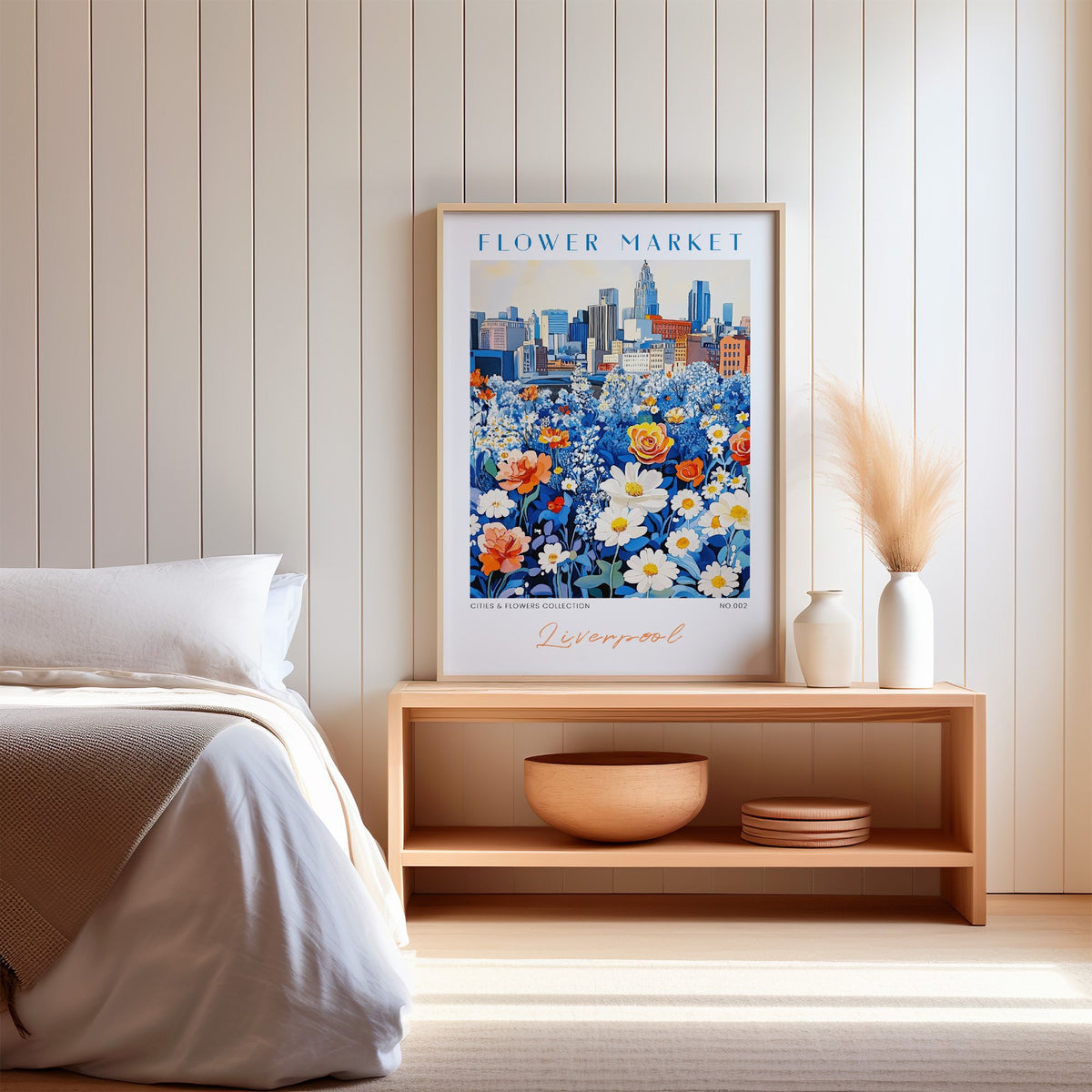 Liverpool flower market print in an oak frame on a wood bench against a white shiplap bedroom wall with pampas grass