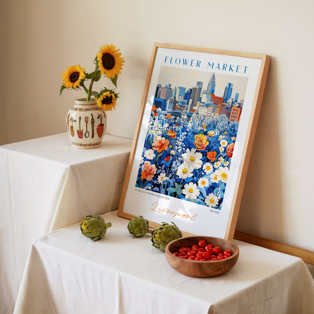 Liverpool flower market print in an oak frame leaning on a linen-draped table beside a vase of sunflowers