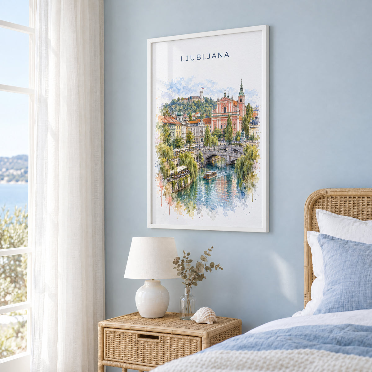 Ljubljana watercolor print in a white frame on a pale blue wall beside a rattan bed in a coastal bedroom