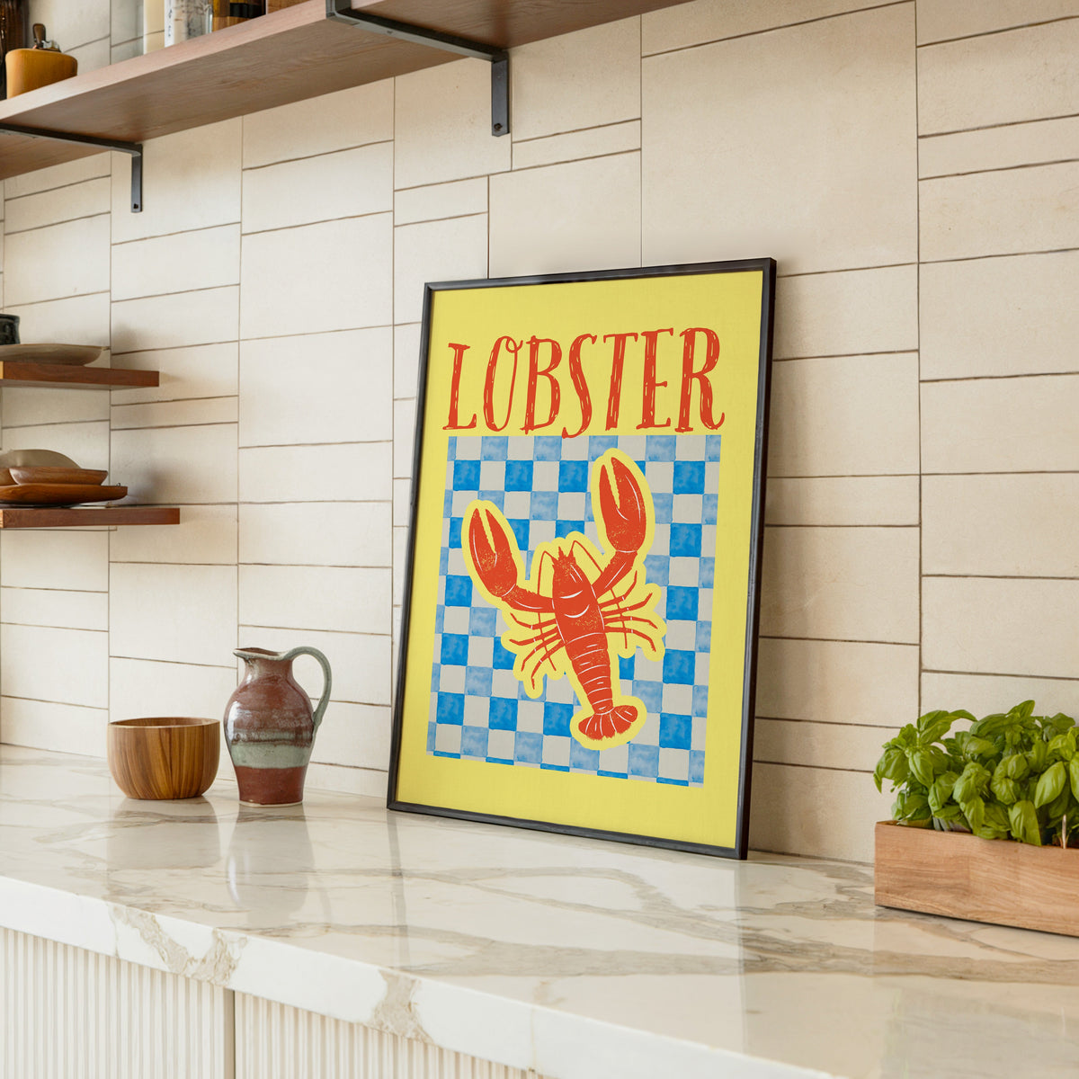 Lobster blue check print in a black frame leaning on a marble counter in a tiled kitchen