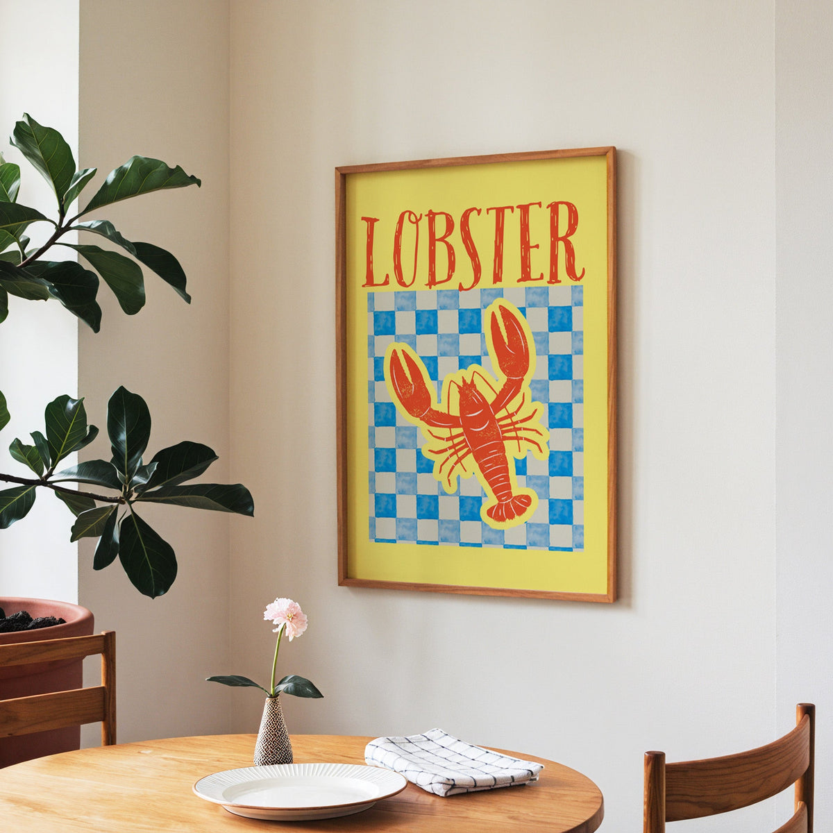 Lobster blue check print in a walnut frame above a round table beside a fiddle-leaf fig
