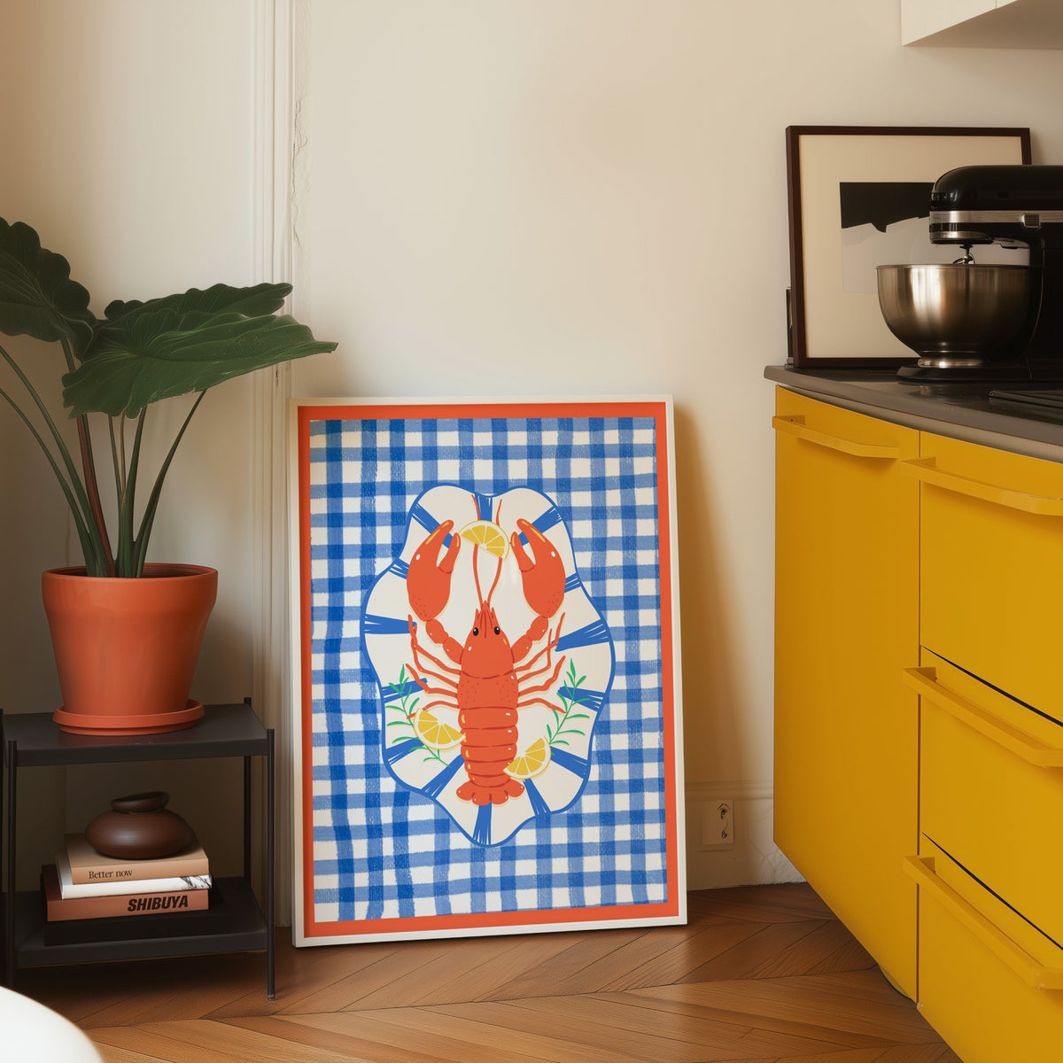 Lobster gingham print in a white frame leaning on parquet beside a bright yellow kitchen
