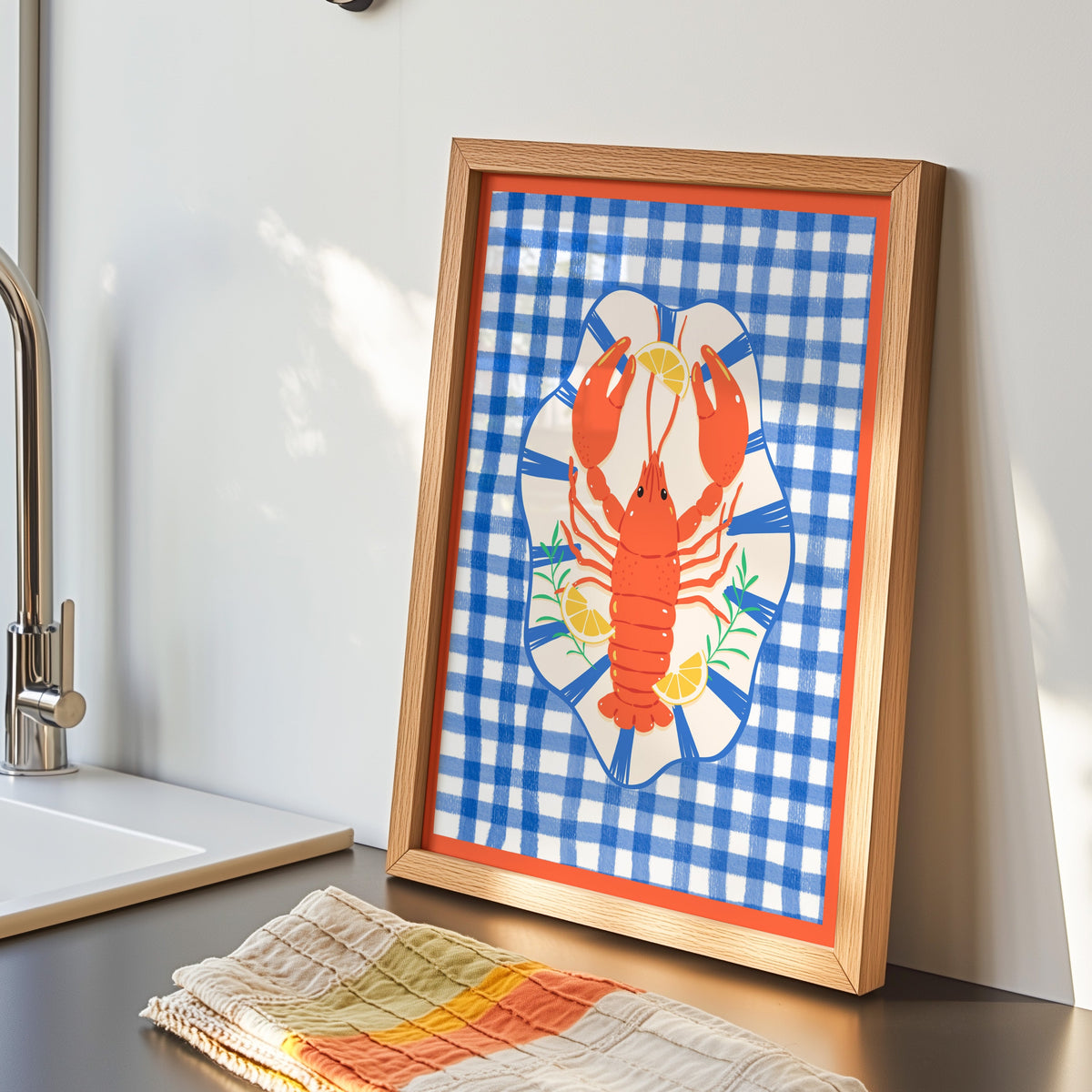 Lobster gingham print in an oak frame by the kitchen sink beside a striped tea towel