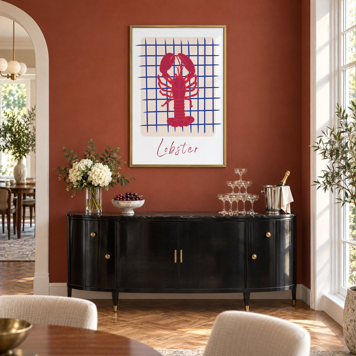 Lobster on cobalt grid print in a brass frame on a terracotta wall above a black buffet with a champagne tower
