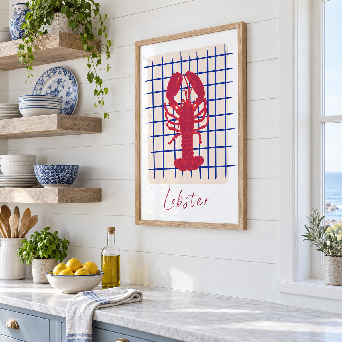 Lobster on cobalt grid print in an oak frame in a white coastal kitchen beside blue and white plates